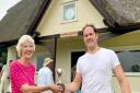 Janet Bazley presents The Colin Bazley Single Wicket Cup to the first winner, Dan Carter. Behind them is the rededicated Clavering Cricket Club pavilion, with the sign reading: The Colin Bazley Pavilion
